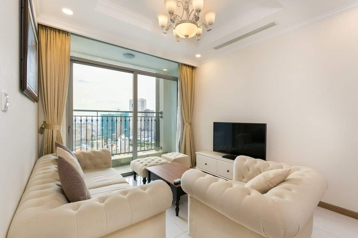 A modern living room with a sofa set, a TV, and a balcony with a city view.