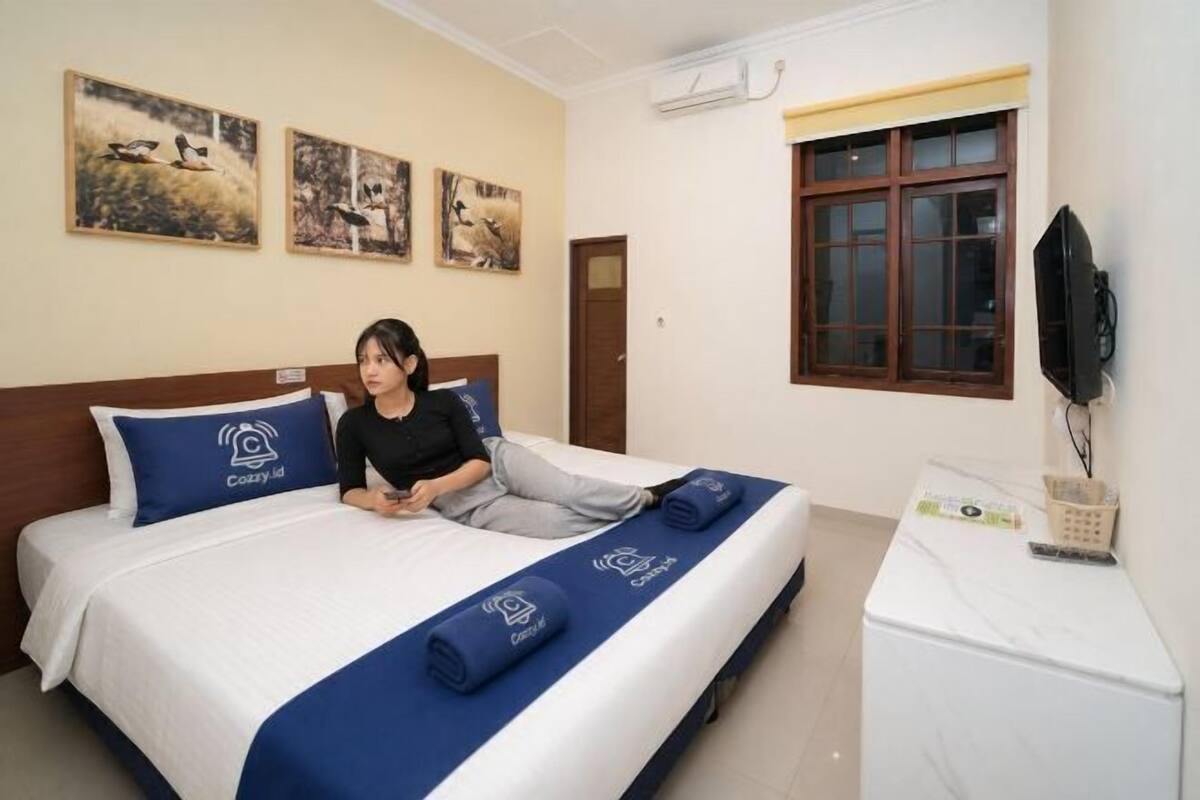 A hotel room with a bed, a television, and artwork on the wall.