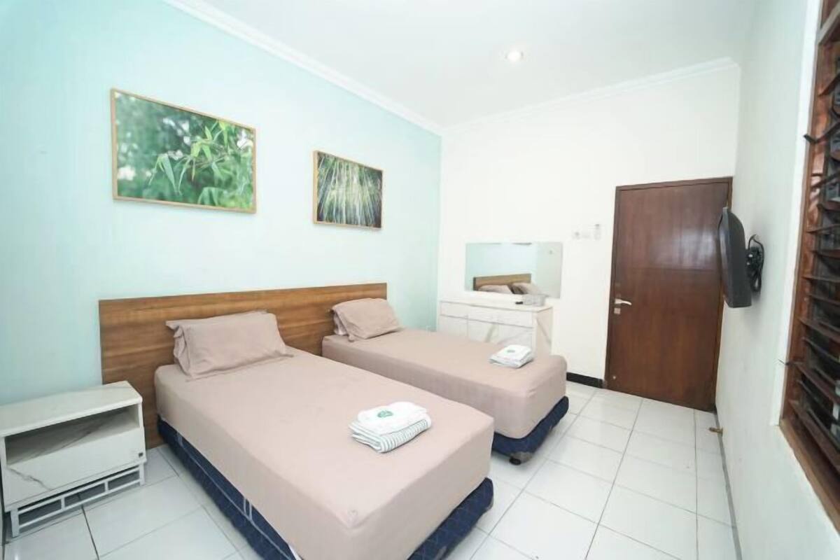 A hotel room with two beds, a bedside table, a wardrobe, and a door with a window.