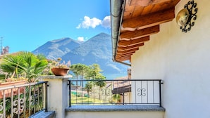A balcony with a view of mountains and the sea, a potted plant, and a decorative wall piece. - Beautiful  villa for 4 people with WIFI, TV, terrace and pets allowed (Porlezza)