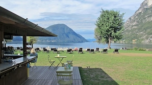 A deck with outdoor seating, a bar, and a view of a lake and mountains. - Beautiful  villa for 4 people with WIFI, TV, terrace and pets allowed (Porlezza)