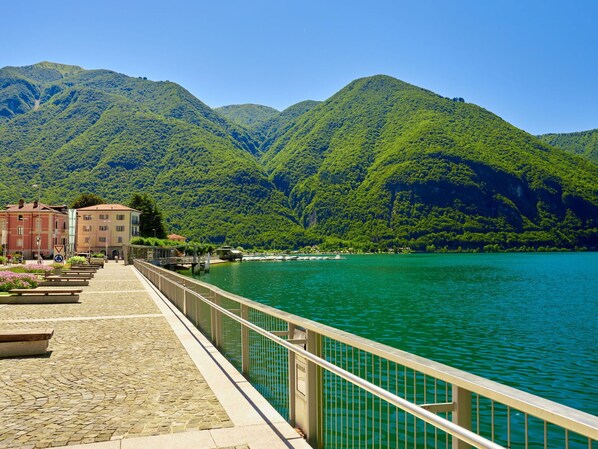 A waterfront promenade with a stone pathway, metal railing, and buildings in the background.
