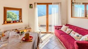 A cozy room with a wooden ceiling, a red sofa, a table with a checkered tablecloth, and a window with a view of greenery. - Beautiful  villa for 4 people with WIFI, TV, terrace and pets allowed (Porlezza)