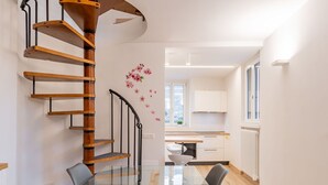 A modern kitchen with white cabinets, a wooden staircase, and a dining area with a glass table and chairs. - Beautiful apartment for 6 guests with TV and patio (Arco)