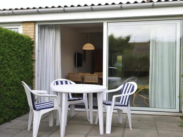 A patio with a round table and four chairs, a sliding glass door, and a TV mounted on the wall. - Holiday Home With Adjacent Views (Nexø)