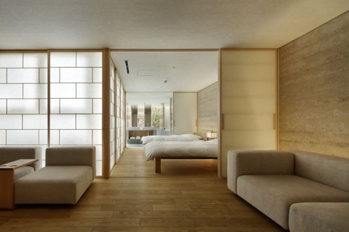 Una habitación de hotel moderna con suelo de madera, un sofá, una cama y un ventanal con vistas.