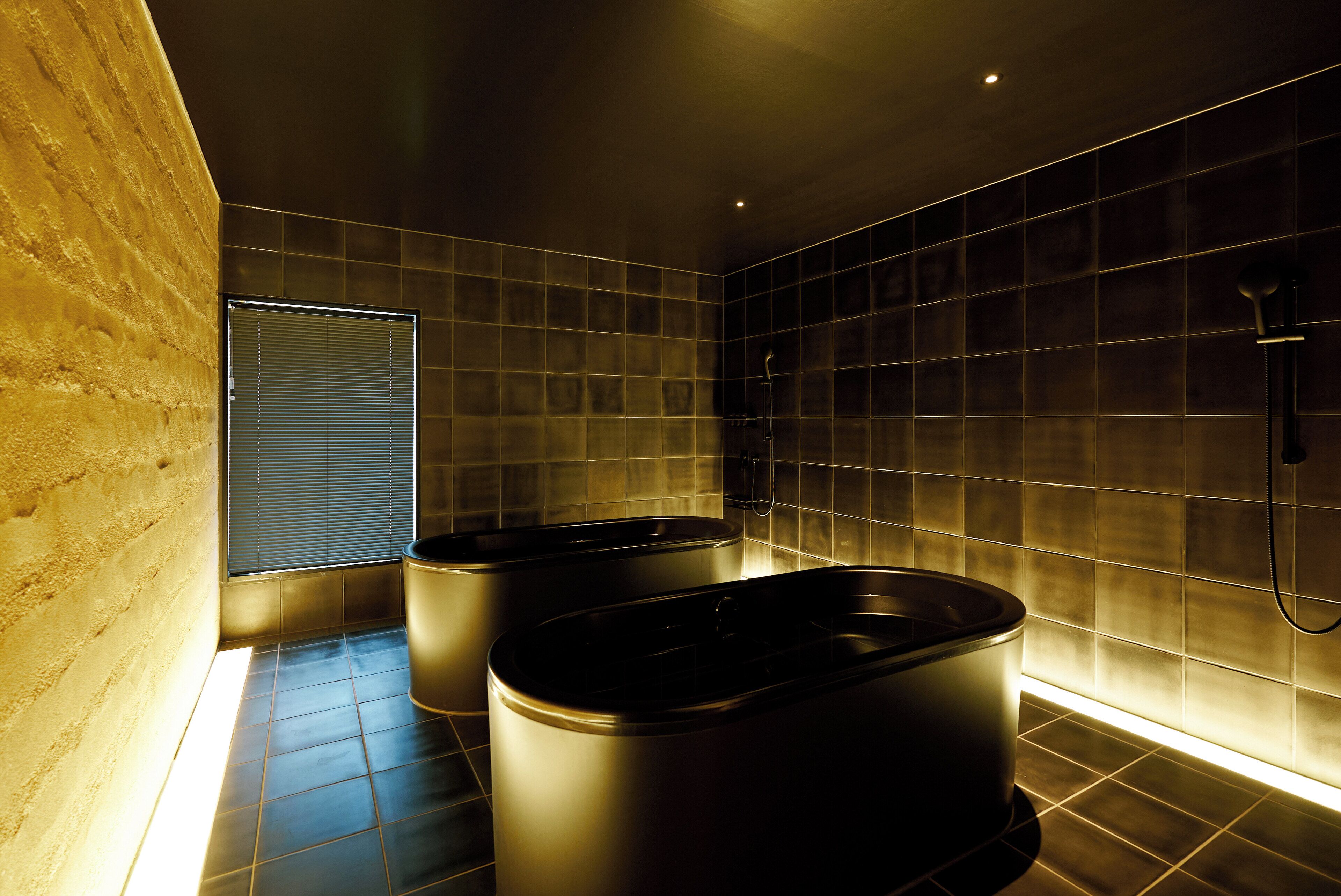 Een moderne badkamer met twee ruime badkuipen, een raam met zonwering en betegelde wanden.
