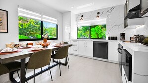 A modern kitchen with white cabinetry, a dining table set for four, and large windows offering a view of lush greenery. - Calm Miami Oasis -Secluded Patio (Miami)