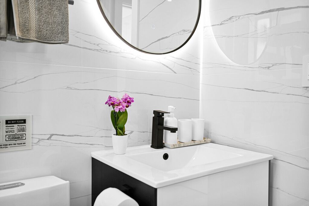 A modern bathroom with a white marble sink, a black faucet, and a potted purple flower.