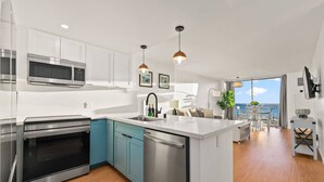 A modern kitchen with stainless steel appliances, teal cabinetry, and a large island.