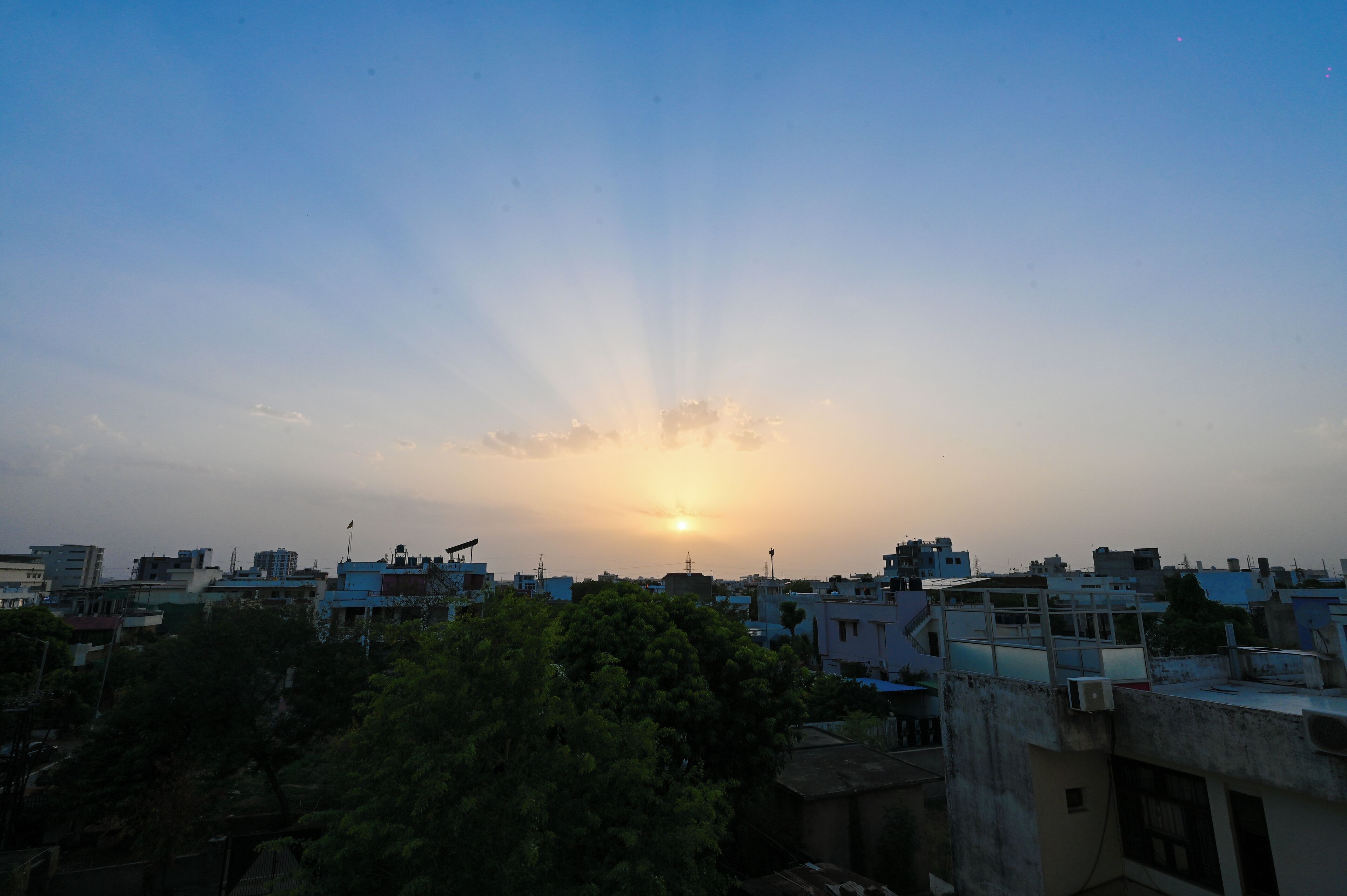 A cityscape at sunset with buildings and trees in the foreground.