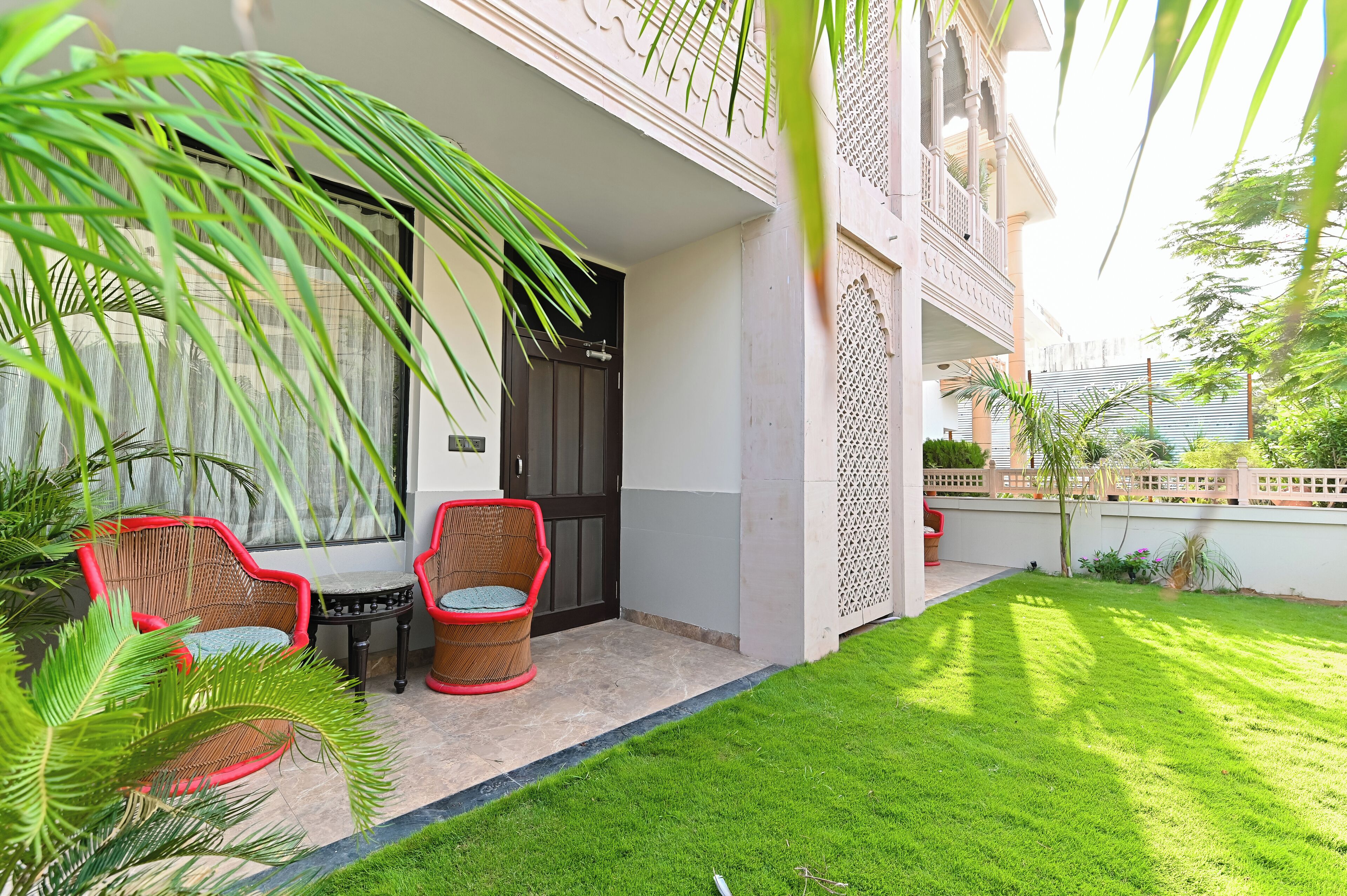 A well-maintained outdoor area with a neatly trimmed lawn, two wicker chairs, a small table, and a door leading to a building with traditional architectural elements.