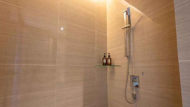 A shower with a handheld showerhead and a wall-mounted control panel. There is a shelf with two bottles. - Greystone 99 Suites (Malacca City)