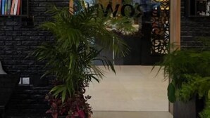 Entrada de un edificio con un gran logotipo 'B', una puerta de cristal y plantas de interior.