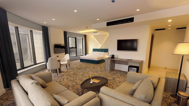 Habitación de hotel con una cama grande, un sofá, un escritorio, un televisor y una ventana con cortinas.