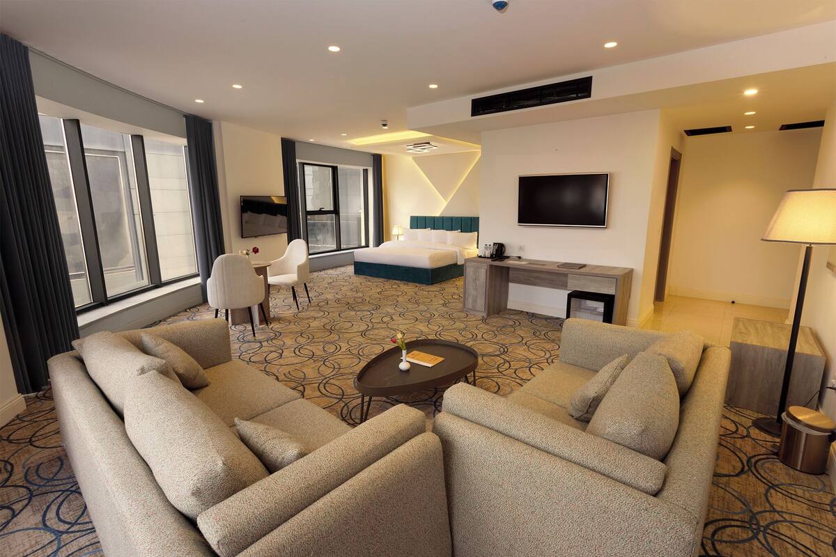 A hotel room with a large bed, a sofa, a desk, a TV, and a window with curtains.