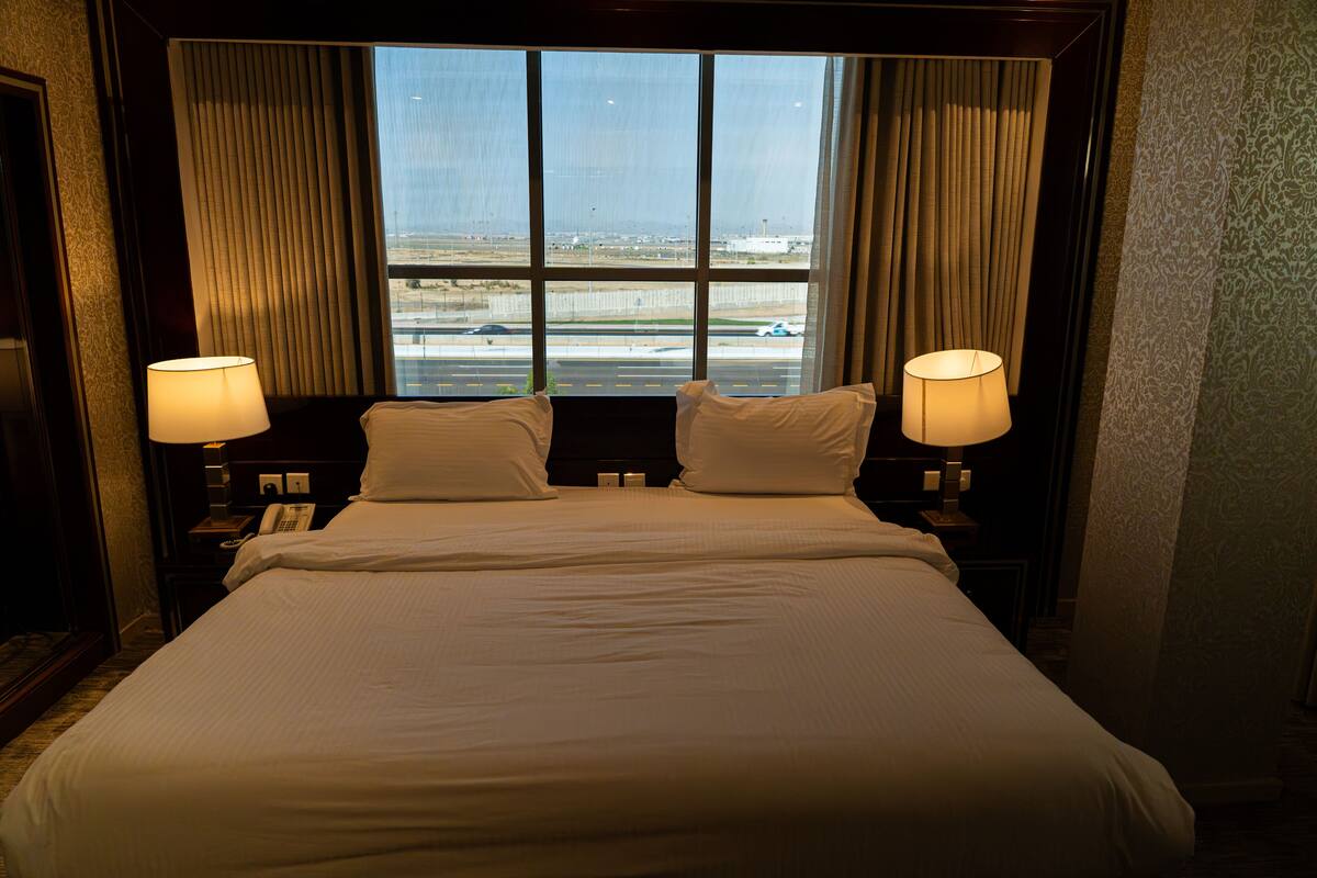 A hotel room with a large bed, two bedside lamps, and a view of a road and buildings through the window.
