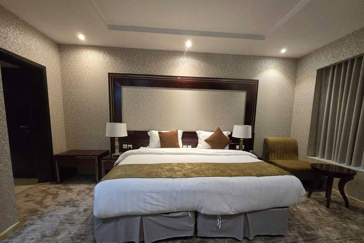 A hotel room with a large bed, two bedside tables with lamps, a chair, and a window with curtains.