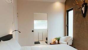 A modern hotel room with a large bed, a sitting area with a chair, a small table with a lamp, and a mounted animal skull on the wall. - Spacious, sunny luxury vacation home with sauna and garden! (Gistel)