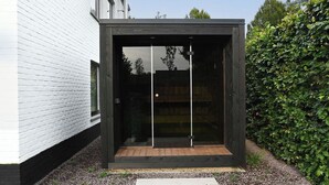 A modern, enclosed outdoor space with a wooden floor, glass doors, and a black exterior. - Spacious, sunny luxury vacation home with sauna and garden! (Gistel)