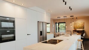 A modern kitchen with built-in appliances, a central island, pendant lighting, and a view of the outdoors. - Spacious, sunny luxury vacation home with sauna and garden! (Gistel)