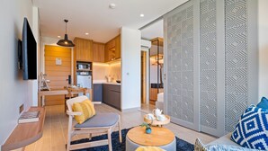 Un salon moderne avec un canapé, une table basse et un téléviseur. Il y a également un coin cuisine avec des meubles en bois et un four à micro-ondes.