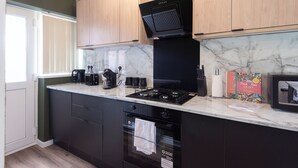 A modern kitchen with dark cabinetry, a black range hood, a marble backsplash, and a built-in oven.