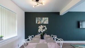 A dining area with a marble table, white chairs, a vase of flowers, and a painting on the wall.
