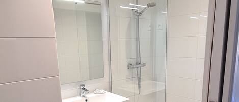 A modern bathroom with a glass-enclosed shower, a white sink, and a wooden floor.