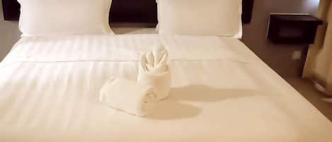 A neatly made bed with white linens, a folded towel, and a dark headboard.
