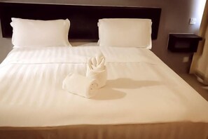 Una cama bien hecha con sábanas blancas, una toalla doblada y un cabecero oscuro.