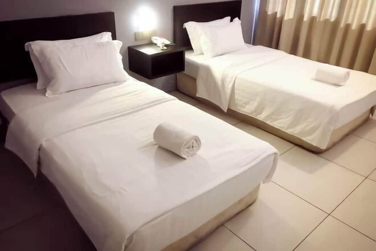 Ein Hotelzimmer mit zwei Betten, jeweils mit weißer Bettwäsche und Kissen, einem Nachttisch mit Telefon und einem Fenster mit Vorhängen.