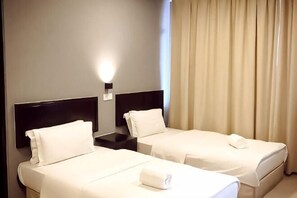 Dos camas individuales con sábanas blancas, una mesita de noche con lámpara y una ventana con cortinas.