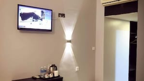Ein Hotelzimmer mit einem an der Wand befestigten Flachbildfernseher, einem kleinen Tisch mit Stuhl, einem Nachttisch mit Lampe und einer Klimaanlage.