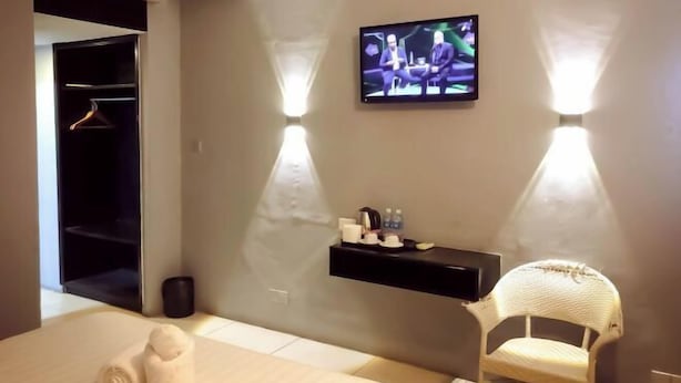 Ein Hotelzimmer mit einem Bett, einem an der Wand befestigten Fernseher, einer kleinen Ablage mit Pflegeprodukten und einem weißen Stuhl.