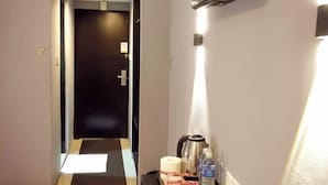 Ein Hotelgang mit einer dunklen Tür am Ende, einem an der Wand befestigten Fernseher und einem Tablett mit Wasserkocher, Wasserflasche und Taschentüchern.