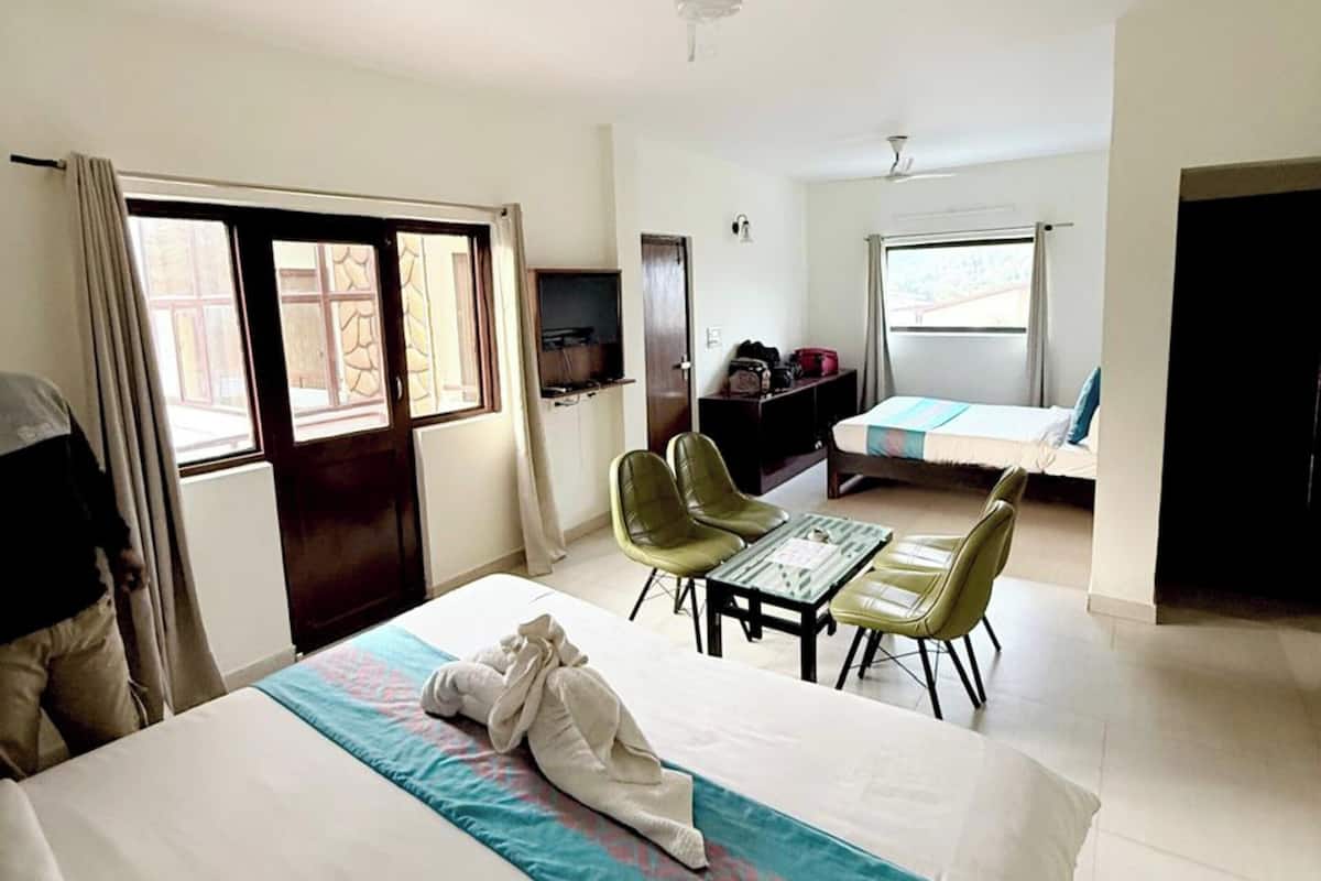 A hotel room with a bed, a desk, two chairs, a ceiling fan, and a window.