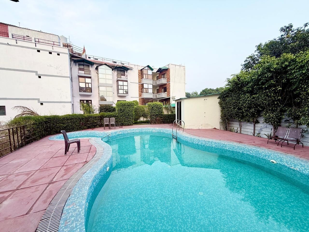 Una piscina con borde de azulejos, rodeada por una zona pavimentada con dos sillas de descanso.