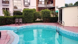 Ein Schwimmbecken mit Fliesenbordstein, umgeben von einem Gebäude mit mehreren Balkonen und einer flachen Dachterrasse.