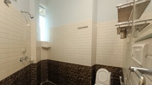 Een badkamer met witte betegelde muren, een marmeren vloer, een douche en een toilet.