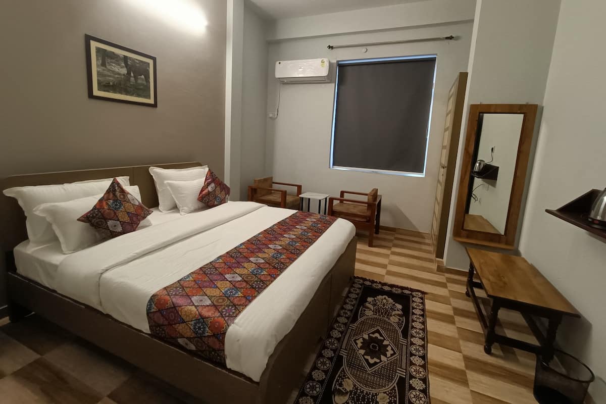Une chambre à coucher comprenant un lit, une table de chevet en bois, une chaise, une petite table, un miroir et une fenêtre donnant sur un paysage.