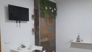 Een moderne woonkamer met een flatscreen televisie aan de wand, een witte eettafel met stoelen en een glazen salontafel.