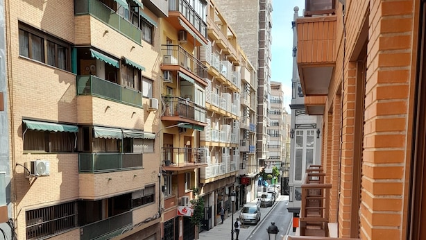 Een meerlaags woongebouw met balkons, airconditioners en een voetgangersstraat.
