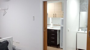 Een moderne woonkamer met een grijze bank, een houten vloer, en een keuken die zichtbaar is door een open deur.