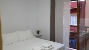 Een moderne slaapkamer met een groot bed, een plafondventilator en een klein nachtkastje met een plant.