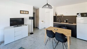 Een compacte keuken met een eethoek, witte kastjes, een flatscreen-tv en een hanglamp.