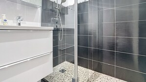 Een moderne badkamer met een glazen douchecabine, een witte wastafel en donkere betegelde wanden.
