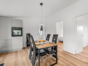 Eine moderne Küche mit eingebautem Backofen, ein Essbereich mit Holztisch und schwarzen Stühlen sowie eine Pendelleuchte.