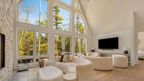 A spacious living room with large windows, a fireplace, and a flat-screen TV. - Luxe Lakefront Home · Sleeps 10 · Jacksonport (Sturgeon Bay)