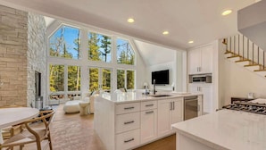 A modern kitchen with large windows, a dining area, and a staircase. - Luxe Lakefront Home · Sleeps 10 · Jacksonport (Sturgeon Bay)